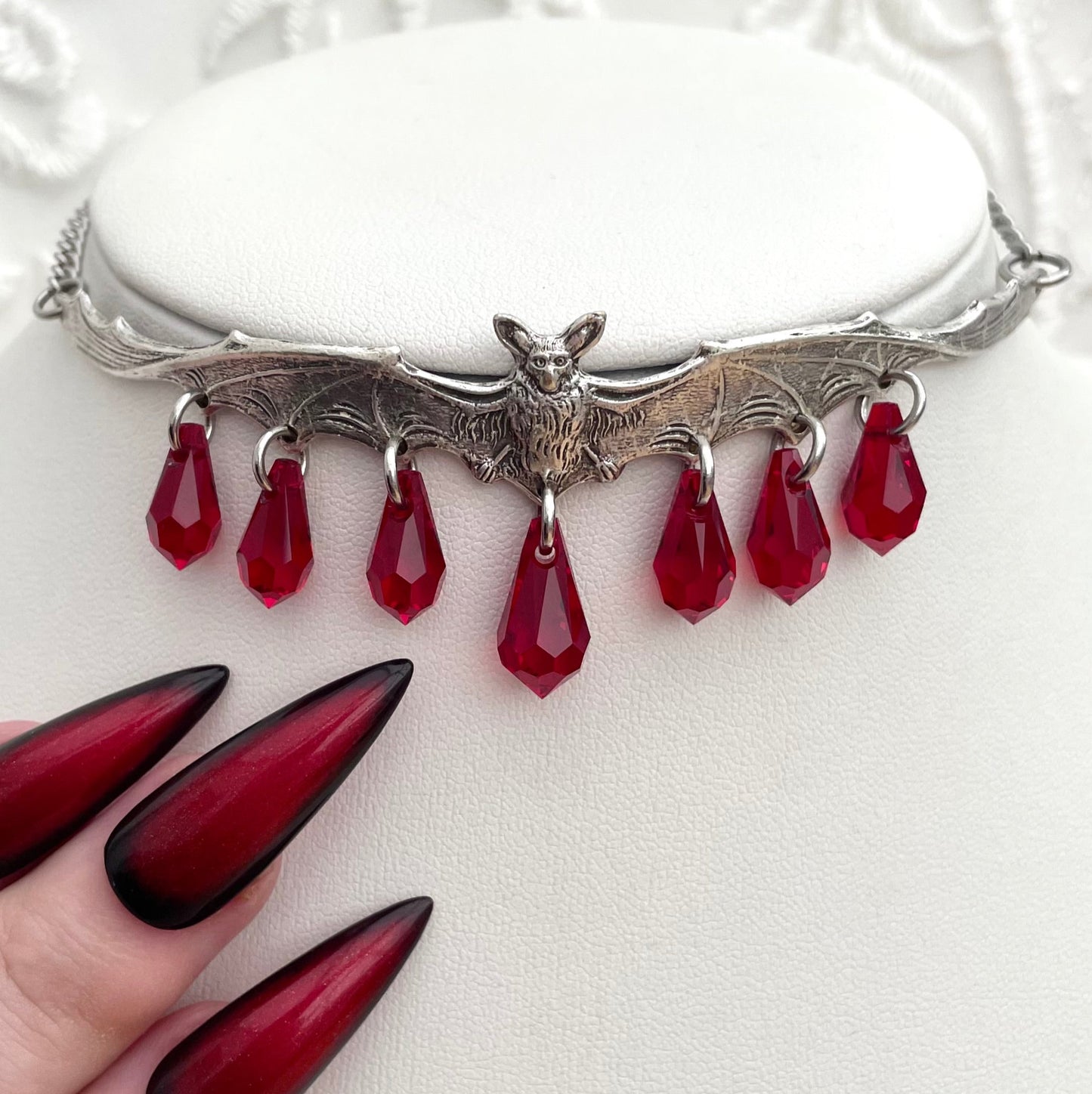Silver necklace with red teardrop pendants on a white textured background